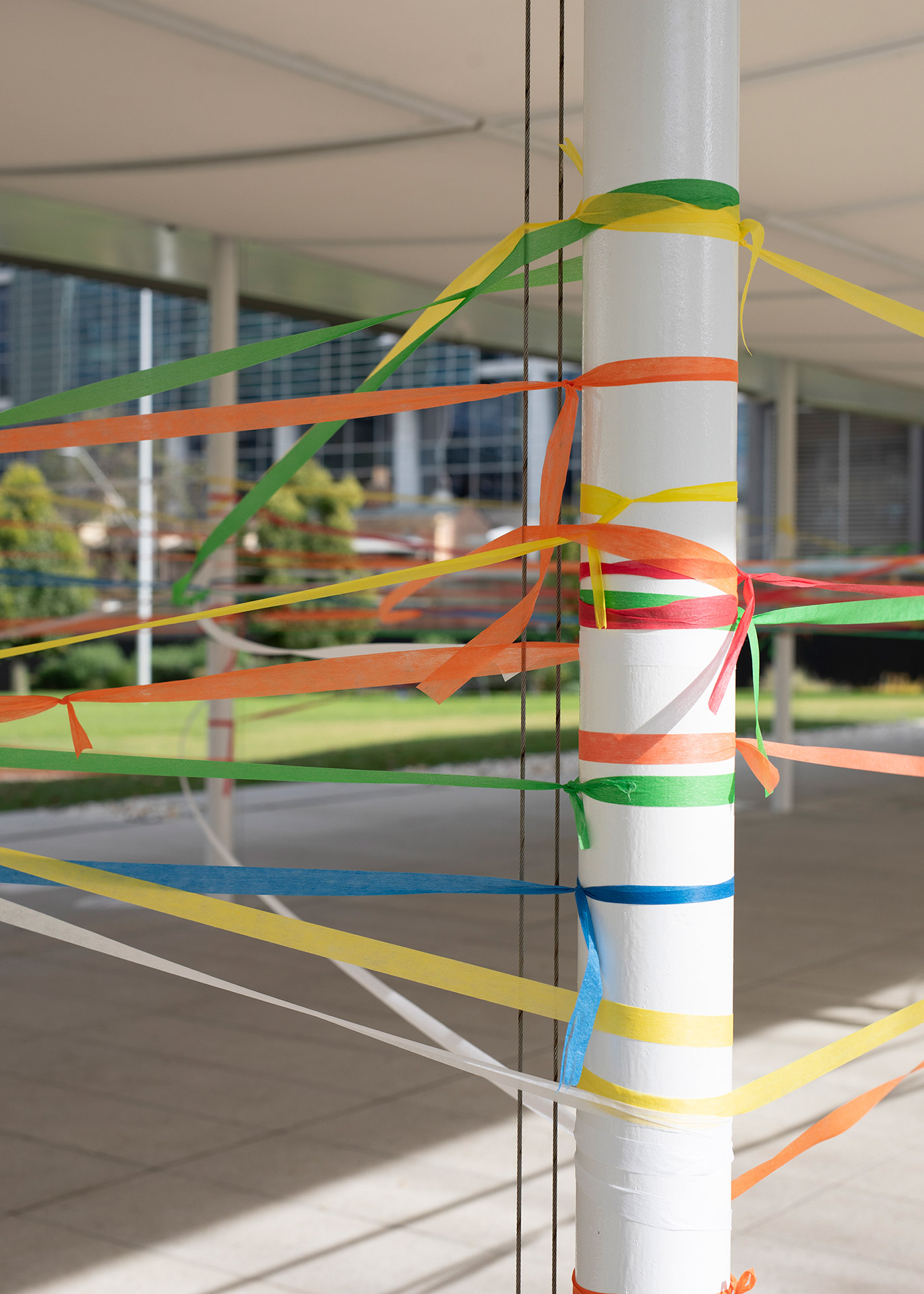 Close-up of a pole with different coloured threads tied to it.