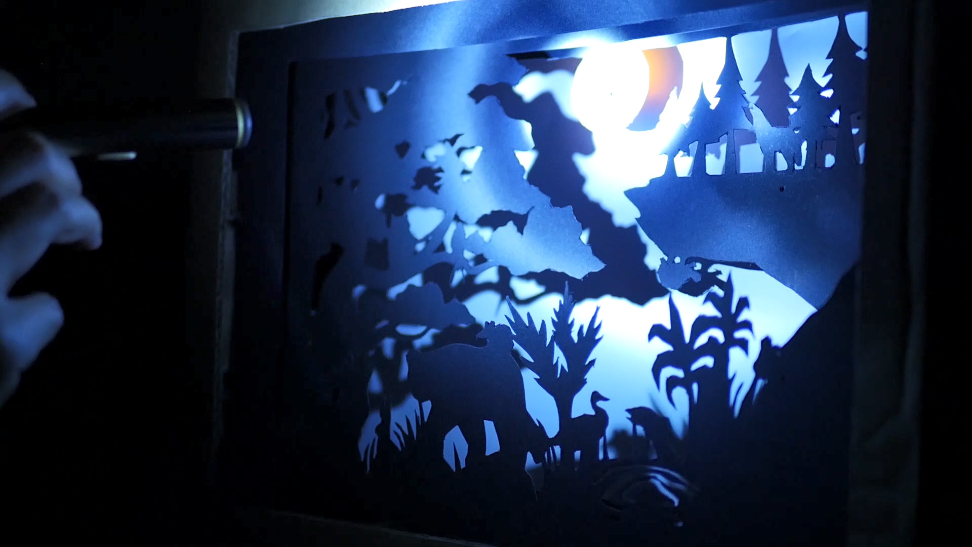 Hand holding torch shining on the moon in the diorama.