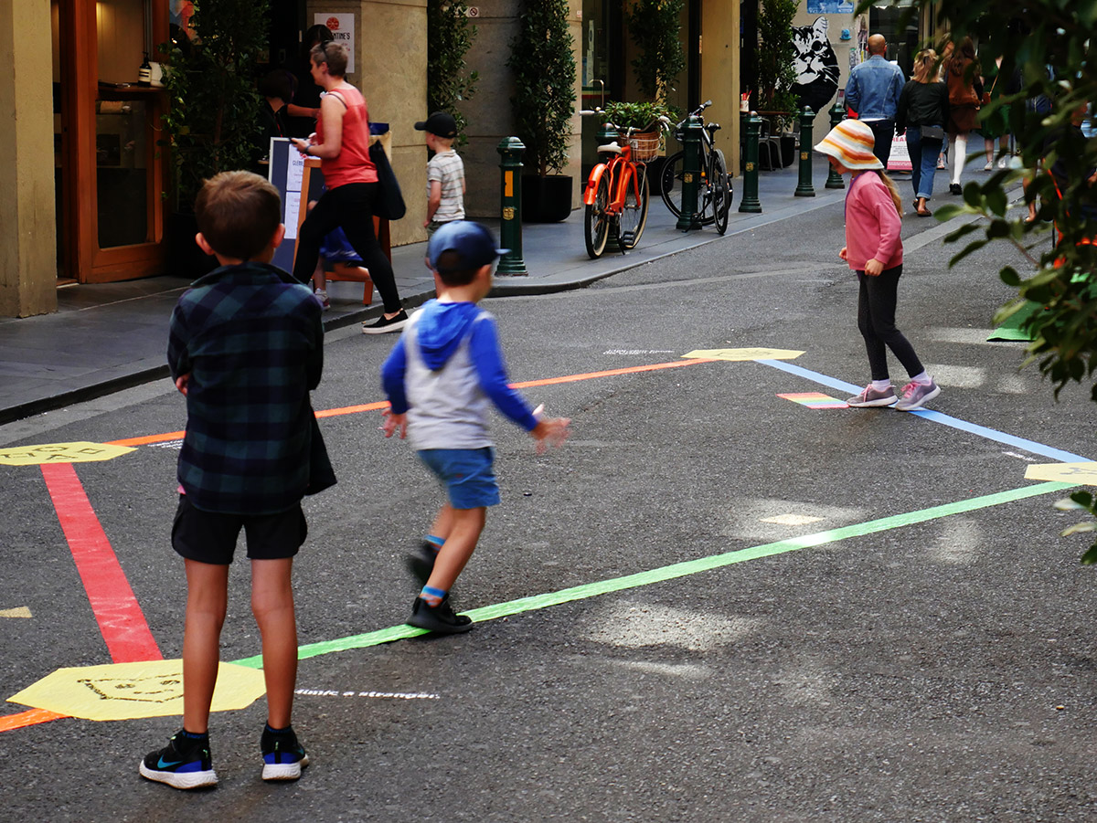 Three children running and playing together on the Rainbow Paths installation on Degraves St.